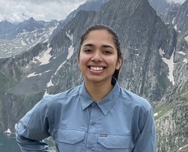 woamn in blue blouse smiling, stangin in fron og mountain range
