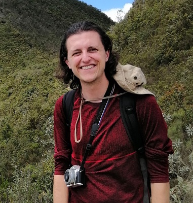 young man in bugundy top mid length dark hair stands in countryside