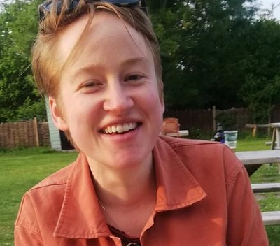 woamn with short hair, sunglasses on her head smiling at camera, wearing an open shirt