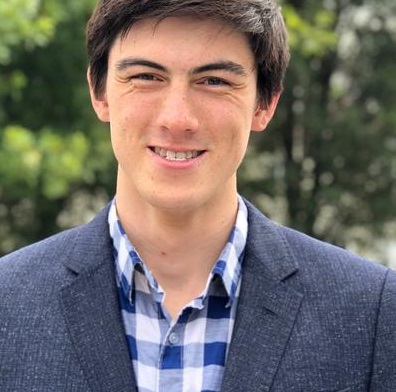 man in blu check shirt and suit jacket. short black hari smiles at the camera