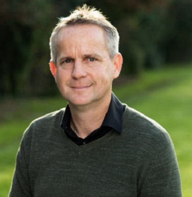 man with black shirt and greay jumper looks at the camera