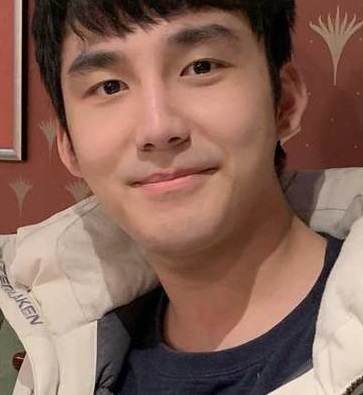 young man short black hari with tshirt and open jacket looks at camera