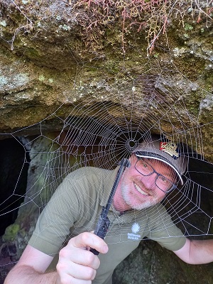 man in a cave looking through spiderweb