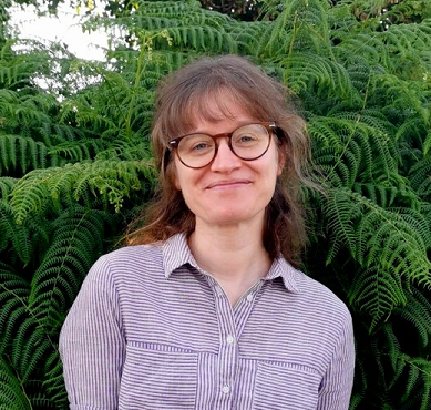 woman with glasses and blouse standing infront of bushes